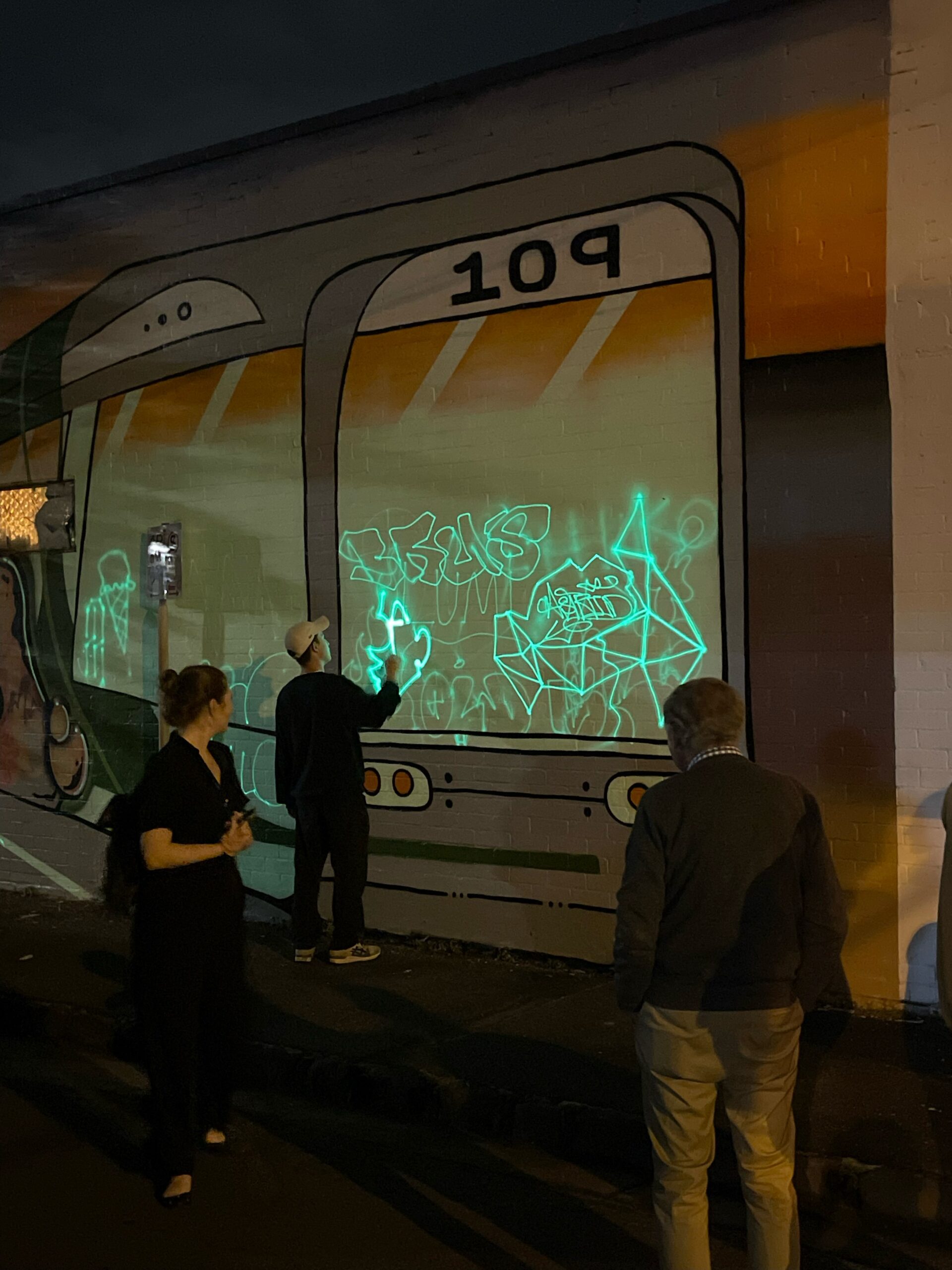 People using light to write on a wall painted with Safety Path photoluminescent paint